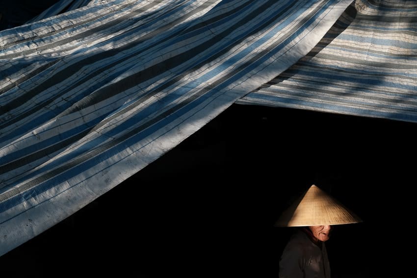 A low key photo of a Vietnamese woman walking under a blue tarp in a market of Vietnam taken during Pics of Asia photography workshop