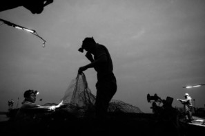 A fisherman's silhouette is seen holding up a net at night with head torch lit