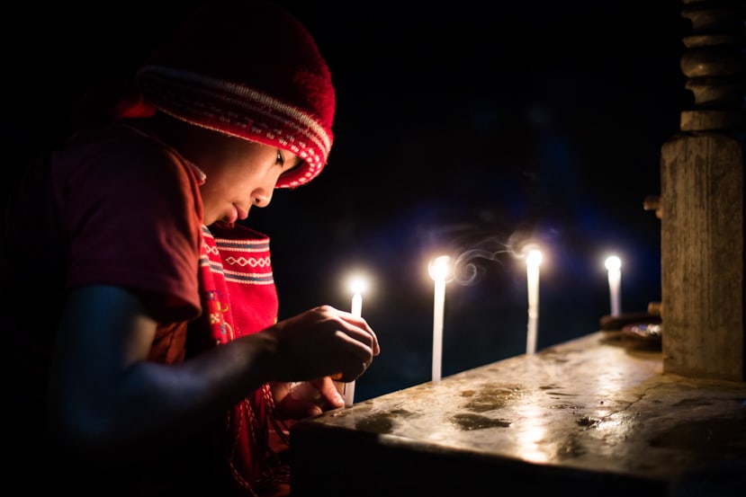 A young man in a red hat lights a prayer candle in a temple in Myanmar - Taken On Tour With Pics Of Asia