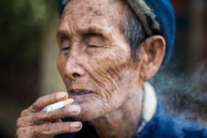 An old man in blue enjoys a long inhale on a cigarette in Central Vietnam - Pics Of Asia Photo Workshop Tours