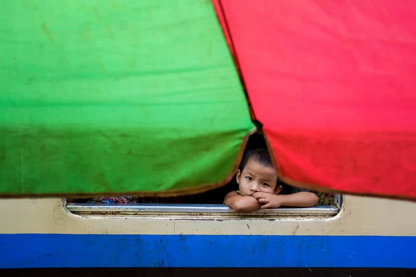 Burmese girl siting on the train behind a green and red umbrella during a Pics of Asia photography tour in Myanmar 