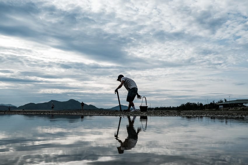 Vietnamese man looking for works in ang Co lagoon mud during a photography tour with Pics of Asia