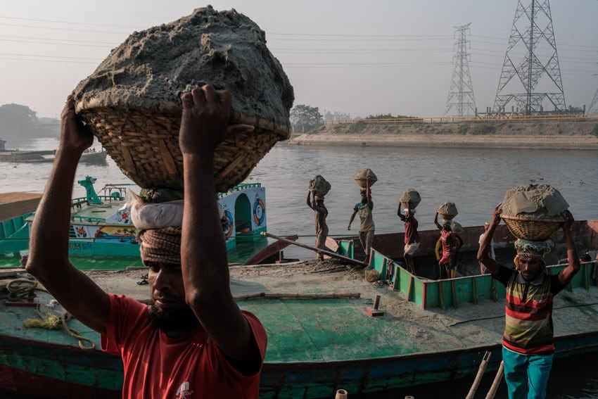 Lines of workers unload sand, rocks and coal from boats along he river in Dhaka, during a photography tour with Pics of Asia