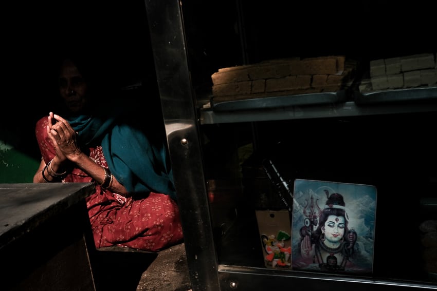 Street photo of an India woman joining her hands next to an image of Shiva in Varanasi, during a photography tour with Pics of Asia