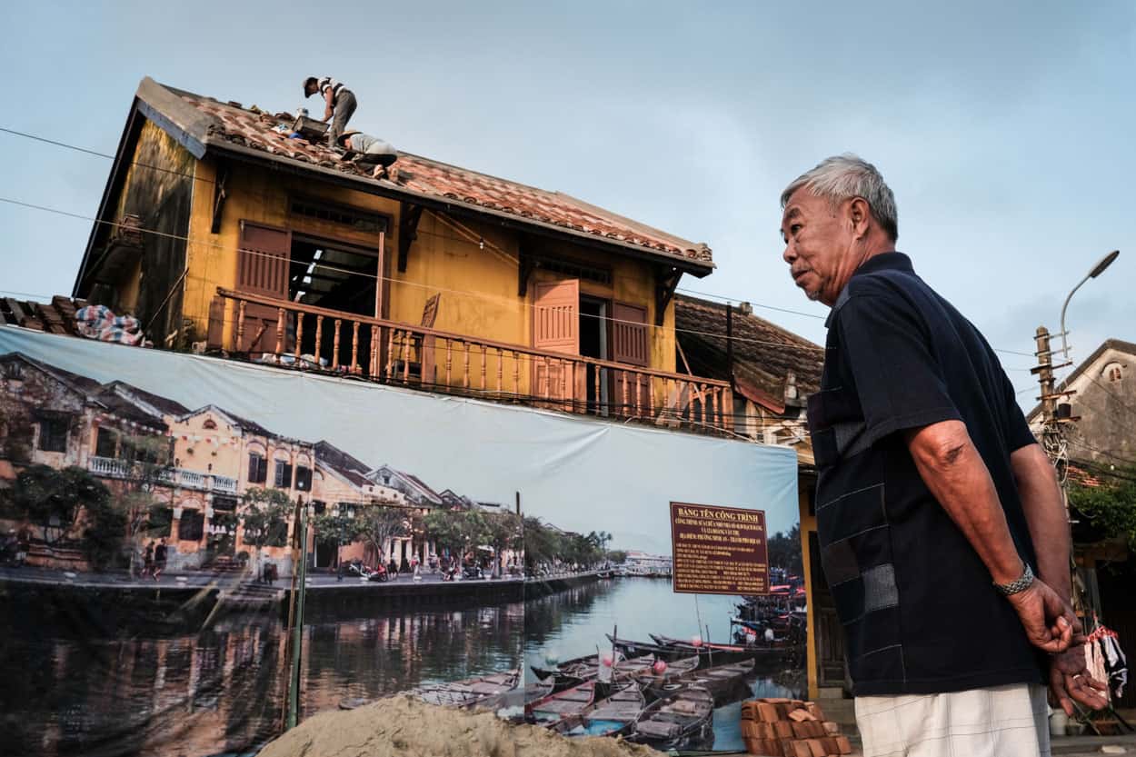 A man looks at workers renovating an old house in Hoi An old town Vietnam