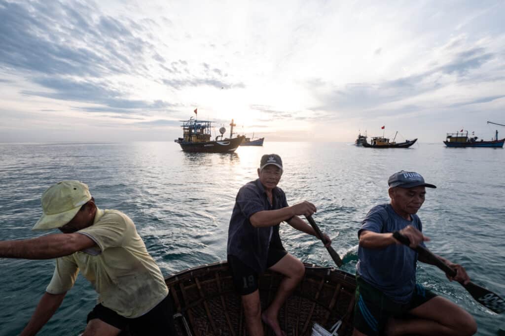 three vietnamese fishermen row their basket boat at sunrise