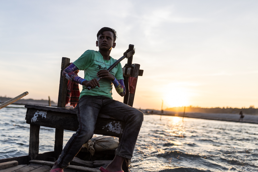 A young boy drives a boat on the river in Bangladesh