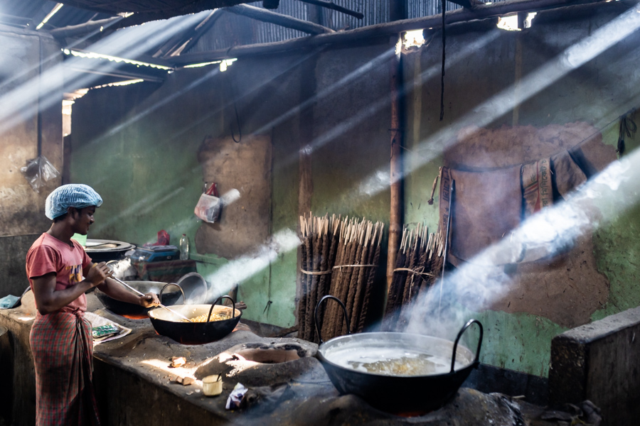 A man cooking in a kitchen with smoke and light beams on a Pics of Asia photography tour in Bangladesh